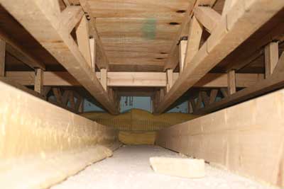 (4) Polyurethane foam adhesive was used to attach gypsum ceiling board to the wooden structural frame in the void space between floors. The floor voids are typically 14 feet × 48 feet × 20 inches per modular unit, which equals approximately 1,300 cubic feet, and may have multiple attached units. It is doubtful that the code developers thought beyond the 1,000-square-foot requirement using the length × width standard when developing the trigger for draftstopping of concealed spaces. Also, note the small dimension finger-jointed truss and the exposed back side of the foam board wall insulation. This void space creates a very effective 