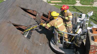 (9) Two firefighters work in unison from the safety of the tower ladder to open up the tepee cut. 