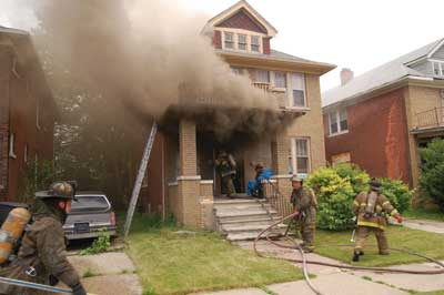 (3) The initial ventilation point at this private-dwelling fire is the front door, which is rarely calculated into the number of ventilation openings that, collectively, impact ventilation-limited fires' tenability. Although the likely location of the fire is the first floor, always check the basement prior to operating above. The presence of board-ups on the basement windows emphasizes this point, as they often conceal fire and smoke conditions. (Photo by Dennis Walus.)