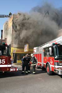 (4) Many cities' truck companies have a roof firefighter position. The roof position allows the IC to get a topside view of the entire fire building through radio reports and can locate any fire showing in the rear and closed shafts much faster than interior companies can. Moreover, this position is able to control ventilation of the interior stairs through the bulkhead door by coordinating this operation with the IC to prevent untenable conditions for those searching for fire inside. (Photo by Tim Olk.)