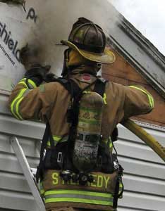 Water is applied from a ground ladder using a 1¾-inch handline from the gable end of the attic to knock down the fire.