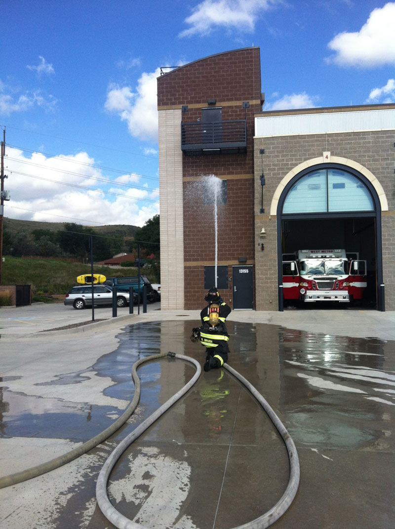 A firefighter trains a hose stream on the exterior of a station.