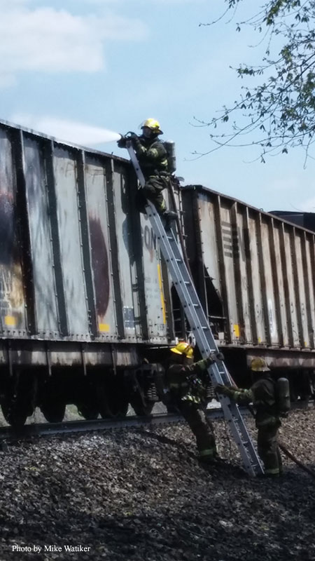 Firefighters ascend a ladder to apply extinguishing agents to a train fire.