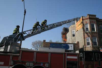 (4) Members of the Chicago (IL) Fire Department make their way to the roof of an isolated three-story multiple dwelling. There is a heavy volume of fire in the rear of the building.