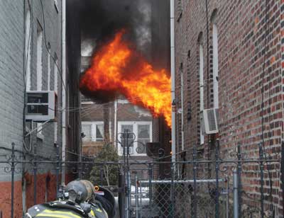 (1) The fire is in the two-story ordinary construction structure. The fire is self-venting out of the first-floor window. The firefighter is getting ready to take the front gate to access the rear yard Allen Epstein 