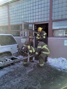 (11) Once clear of the window, the two firefighters will lower the end of the ladder to the ground. The other firefighter drops his arm positioning to the sides and continues holding the ladder at an angle, acting like a pivot point to make lowering easier.