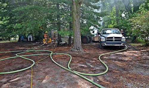 (1) Street view of the A side of the dwelling. The low-hanging branches and overgrown vegetation prevented the first-arriving unit from conducting a windshield size-up, which emphasizes the importance of completing a 360° size-up every time, at every incident. In the foreground are two 1¾-inch hoselines (one attack, one backup) and the yellow electric cord that powered the positive-pressure ventilation fan. <i>(</i>Photos by Bob Bartosz.)