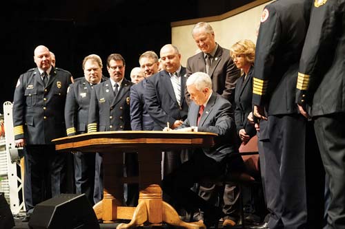 (7) Indiana Governor Michael Pence signs the bill creating the Indiana Fire Training Academy as the bill's sponsors and supporters look on. The facility will offer standardized training, have quality assurance as a priority, foster consistency in training, and have the training continue at district training centers, Pence noted.