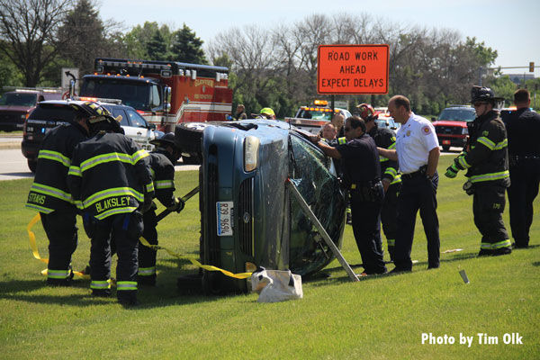 Firefighters stabilize a vehicle that has rolled over while a police officer comforts a patient.