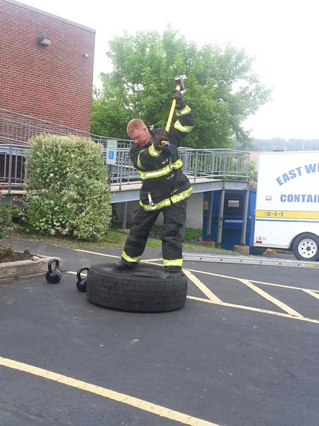 A firefighter swings a sledgehammer while wearing turnout gear as part of a workout.