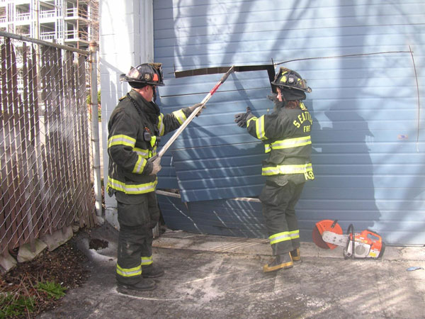 Firefighters force entry on a roll-up door during a training evolution.