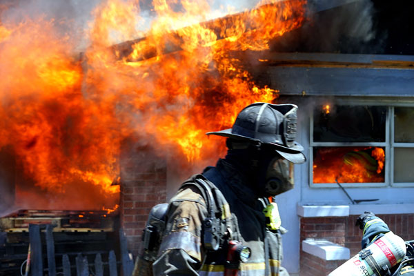 A firefighter stands in front of a burning building during a firefighter training evolution.