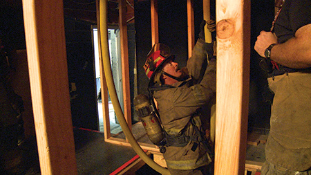 The firefighter to be rescued straddles the hose facing the anchored side.