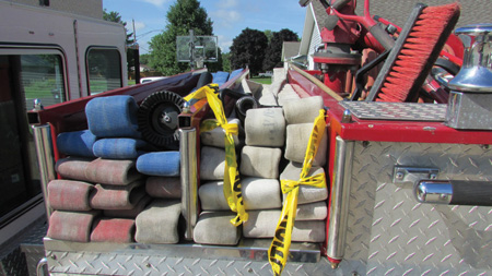 This hose deployment method will work with a standard flat load without strategically placed loops. The firefighter must locate the fold that corresponds to the first coupling (50 feet) from the nozzle. The nozzle loop is the higher marked fold. For this photo, the corresponding folds were marked with scene tape and chalk.