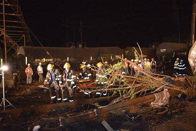 (11) A ladder company used stokes baskets to carry extrication tools to the scene. Responders used stoke baskets with backboards to ferry passengers to the two triage/treatment areas (East and West). Note the close proximity of the stored tank cars to the passenger train wreckage. 