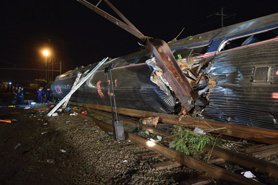 Car 2 lies on its side. A catenary pole penetrated its stainless-steel body. Portable battery-powered LED lighting illuminates the scene. Responders used numerous portable ladders to access the windows of each of the four overturned rail cars. Portable generators and hydraulic extrication equipment are staged outside the car.