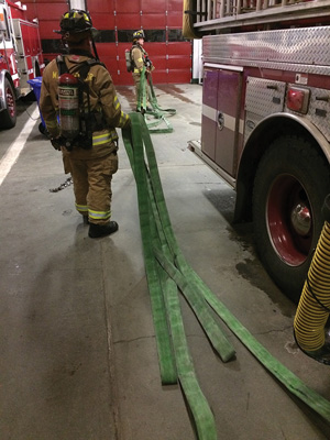 (3) When deploying with two firefighters, the first firefighter reaches through the top two pulling loops and walks away from the apparatus, allowing the hose to be dragged behind them. The firefighter needs to control the nozzle with his opposite hand as he pulls out the line.