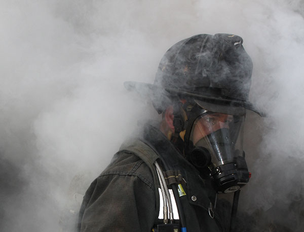 A firefighter wearing SCBA moves through smoke.