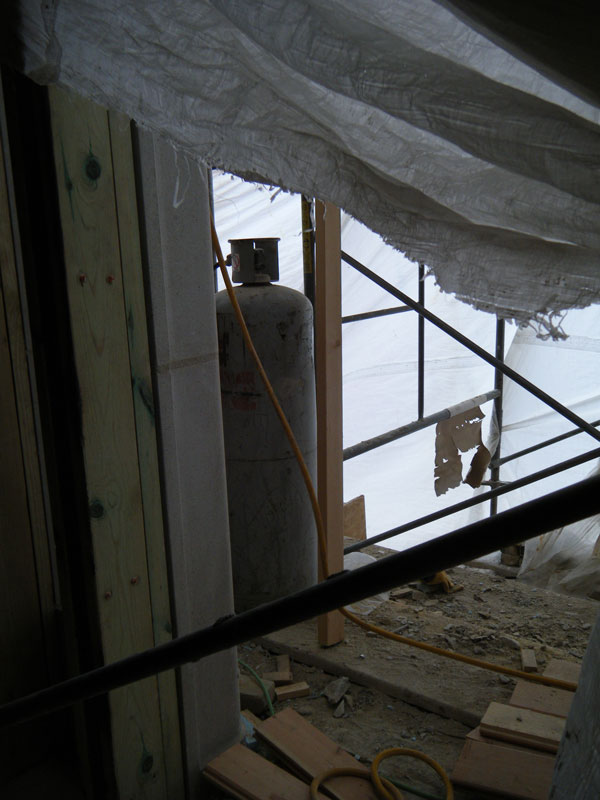 An unrestrained 100-pound (45 kg) propane (LP) cylinder located on a scaffold platform inside a heated winter enclosure that is an extension of an upper floor of a wood-frame building.