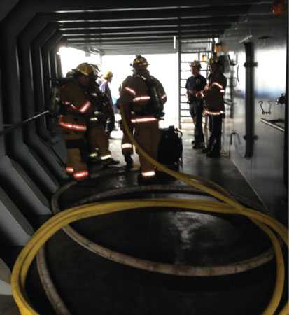 Firefighters deploy a hoseline into the ship’s laundry as they ventilate the spaces, providing the vessel’s crew with breathing air and protecting them in place.