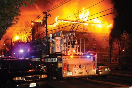 (6) This photo, taken near the corner of Building A, shows the difficulty firefighters had accessing the fire building even from the public street because of the congestion from cars parked on both sides of the narrow street. <i>(Photos 6-8 by Keith Addie.)</i>  “></td>
</tr>
<tr>
<td align=