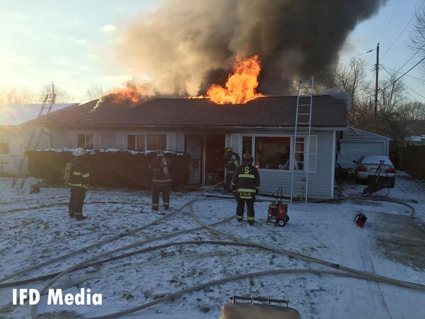 Fire vents from the roof of a single-story home in Indianapolis as firefighters battle the flames.