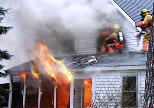 Firefighters operating above flames venting from a house fire.