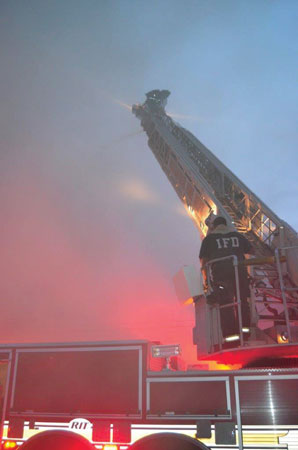 (2) The firefighter on the tip of the ladder is directing the elevated master stream because the apparatus operator’s vision is obscured by the smoke conditions. 