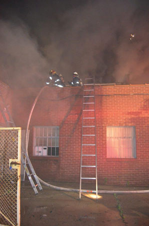 (5) Members position a ladder for a quick escape from the roof of the one-story setback. The firefighters operating the line on the roof need a quick and safe way off the roof if conditions change. 