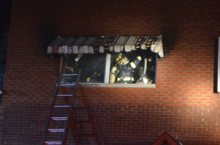 (7) The fire is knocked down; members are overhauling the second floor to check for hot spots. A firefighter places a portable ladder to the second floor as an emergency egress point if necessary.