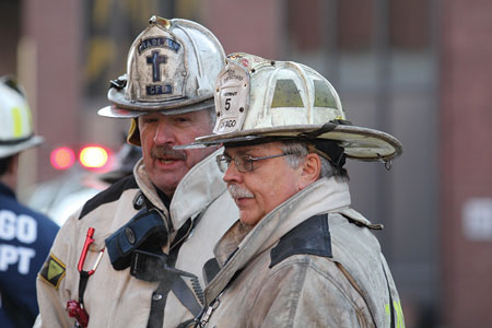 (4) When you need that wall of confidence! Chaplain Father Tom Mulcrone (left) visits with CFD Deputy District Chief Bob McKee at an extra-alarm fire. (Photo by Gordon Nord.)