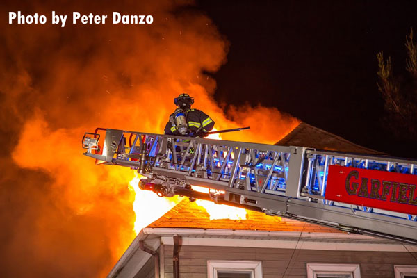 A firefighter on an aerial device as fire vents through the roof at a Garfield house fire.