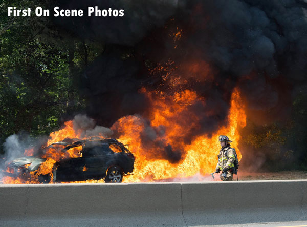 Flames from a car fire rage behind a firefighter responding to the scene.