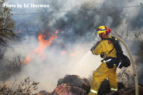 A firefighter trains a hoseline on flames from the Pala Fire near San Diego.