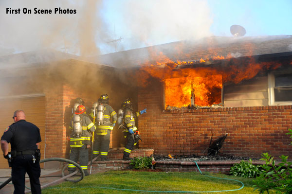 Flames vent from the front of a ranch style home in Baldwin, New York, as firefighters prepare for fire attack.