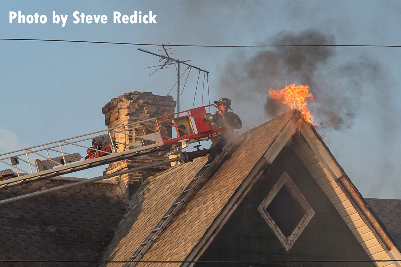 A firefighter performs roof work at a three-alarm house fire in Maywood, Illinois.