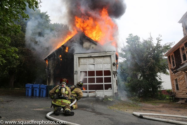 Firefighers train a hoseline on a fire in a garage.