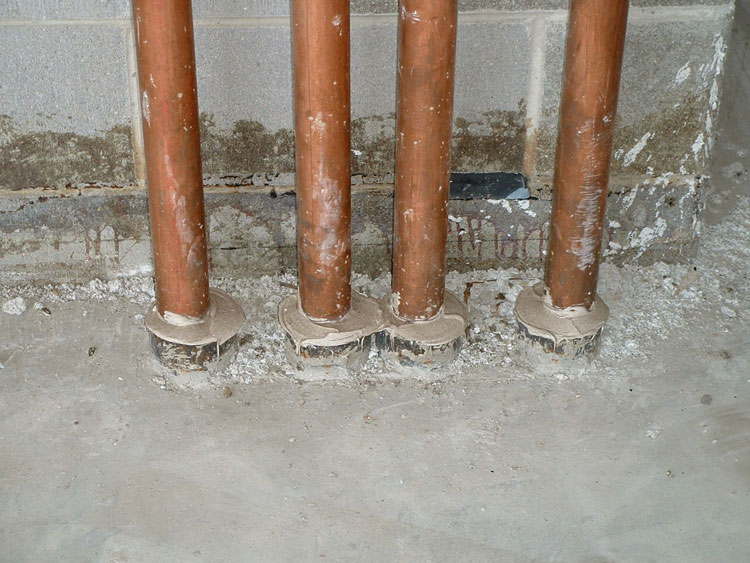 Four pipes penetrating a two-hour-rated structural concrete floor, each with its own steel pipe sleeve.