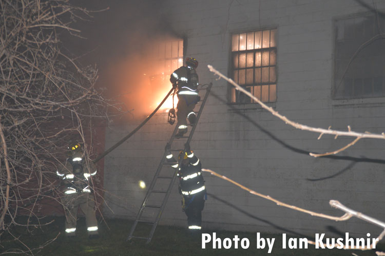 Dearborn firefighter scales a ladder with a hoseline to attack fire.