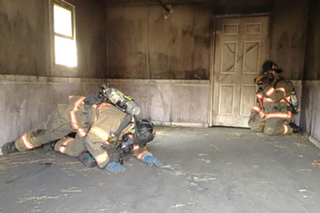 (1) When searching, have the firefighter with the TIC stay at the door. This firefighter will control the door, direct the searching firefighter, and conserve his air supply. <i>(Photo by Chris Baines.)</i>