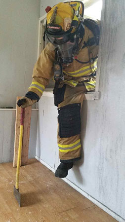 (7) After sweeping the floor with a boot to check for any victims at the windowsill, the search position FF sounds the floor for integrity prior to entering. He uses a flathead ax here to sound the floor, since the halligan was used as a step to enter the room.