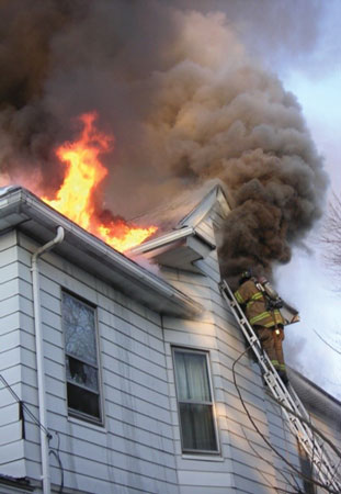 (2) Thick, dark smoke billows out of a dormer window after it is ventilated. The characteristics of the smoke indicate an advanced fire with high heat conditions.