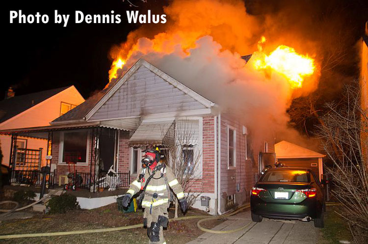 Flames shoot from the roof of a home in Royal Oak, Michigan, as a firefighter walks across the fireground.