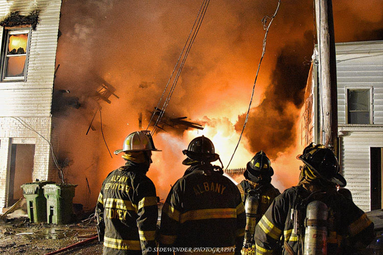 Firefighters at the scene of a fire with flames blazing from a balloon-frame structure in Cohoes, New York.