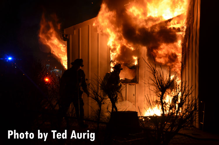 Firefighters outside a home with smoke and fire coming out of the windows.