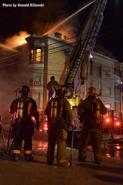 Three firefighters watch as an aerial device sprays water on the exterior of a burning apartment building in Buffalo, New York.