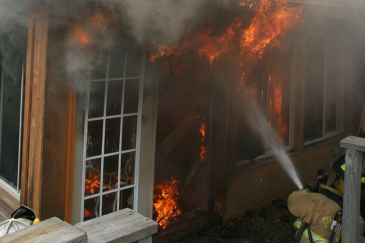 Firefighter applies water to fire through ventilation opening.