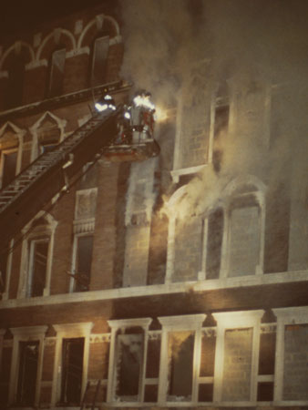 (5) Tower ladders provide a good, safe, and stable platform when firefighters must open up blocked-up windows. Firefighters operating in the bucket must wear the installed safety belts. (Phot<i>os 5-6 by M</i>att Daly.)