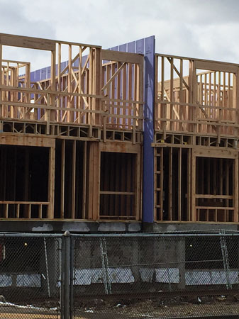 (6) The blue wall in the center of the photo is a gypsum board fire wall, installed in a small gap between two adjacent, structurally independent wood-frame structures under construction; each is built atop a concrete “pedestal.” Once the exterior sheathing and siding are installed, it will be impossible to see the fire wall. The only hint a fire wall is there will be a set of rated fire doors in the middle of the hallway passing through the fire wall. 