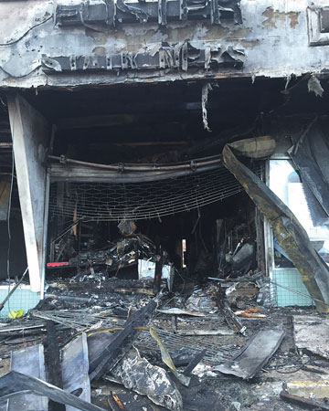 (4) The storefront after knockdown shows a mangled roll-down gate and debris from the collapsed soffit that had to be overcome during the fire attack.<i> (Photo by Jason Lanzilotti.) </i>